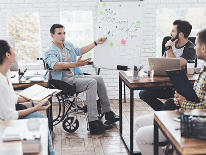 Man in wheelchair presenting to three other people at work