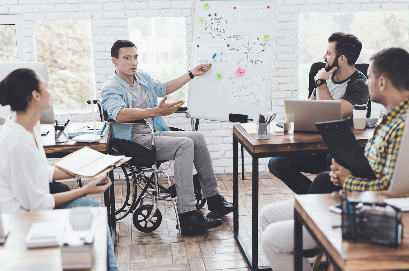 Man in wheelchair presenting to three other people at work