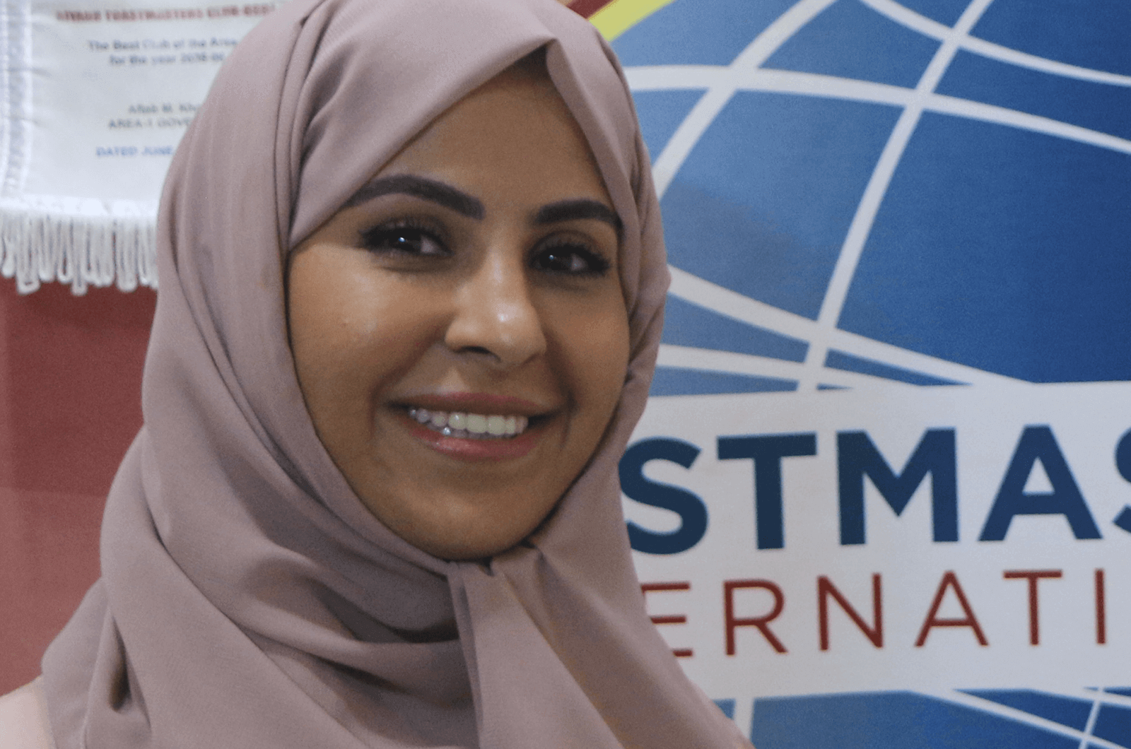 Woman wearing hijab standing in front of Toastmasters banner