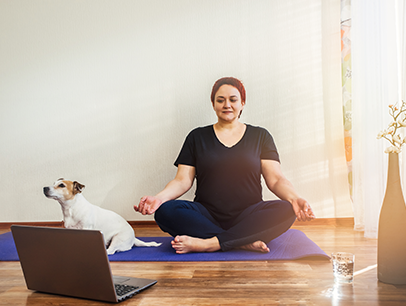 Woman watching laptop and posing on purple yoga mat with a dog