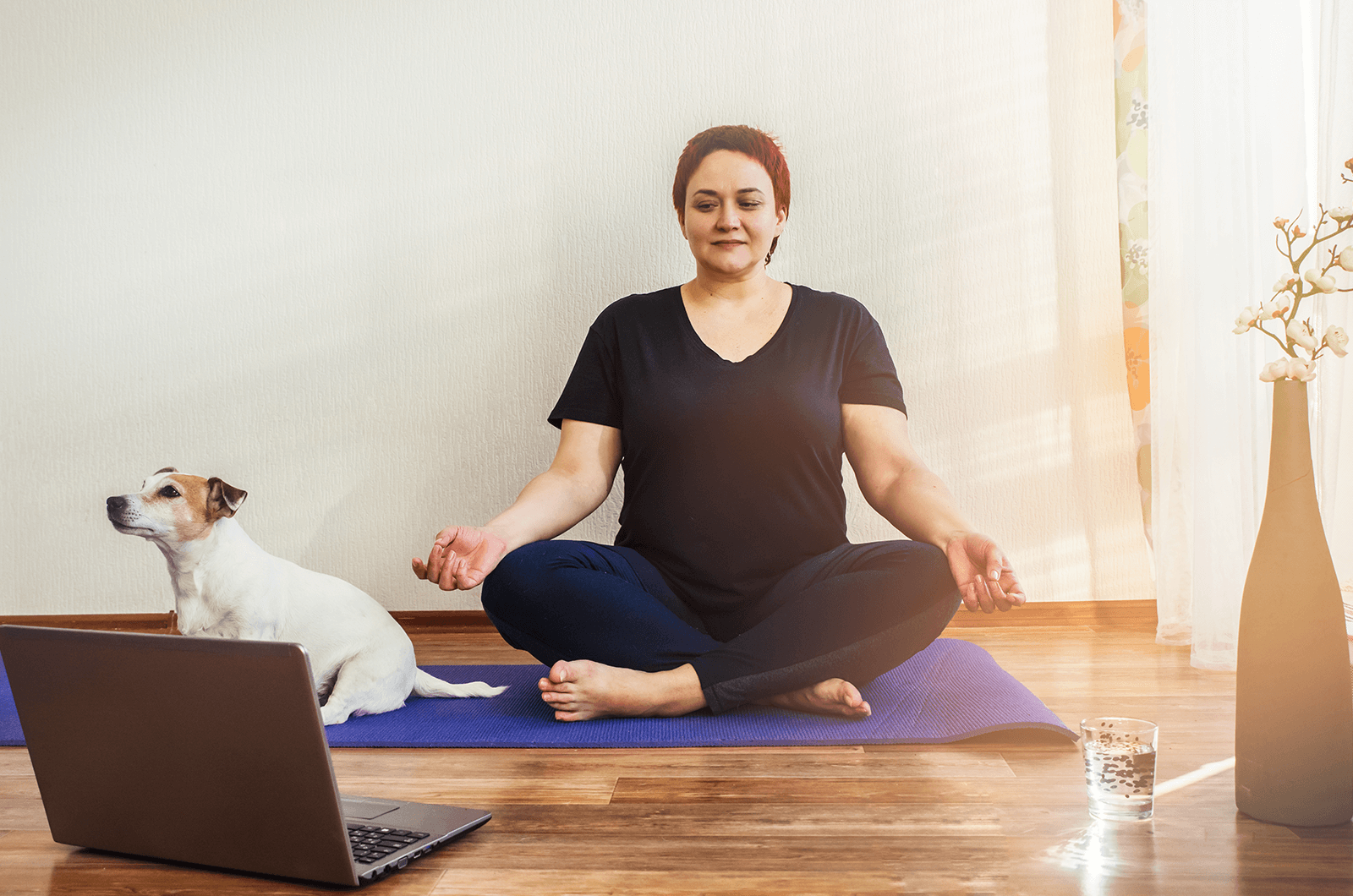Woman watching laptop and posing on purple yoga mat with a dog