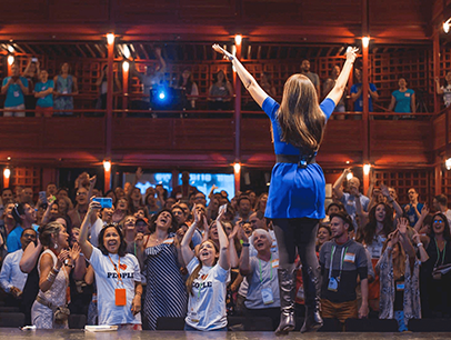 Woman in blue dress onstage with her hands up