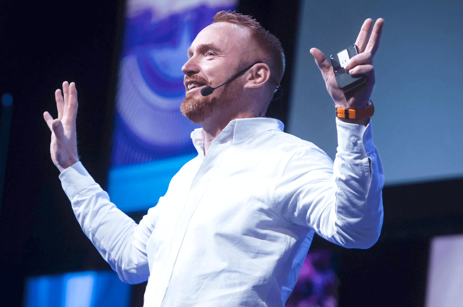 Man in white shirt with hands up speaking into headset onstage