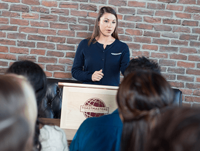 Woman in blue sweater speaking to group from lectern