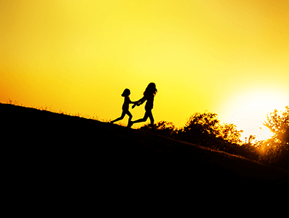 Silhouette of two kids running on hill while sun sets
