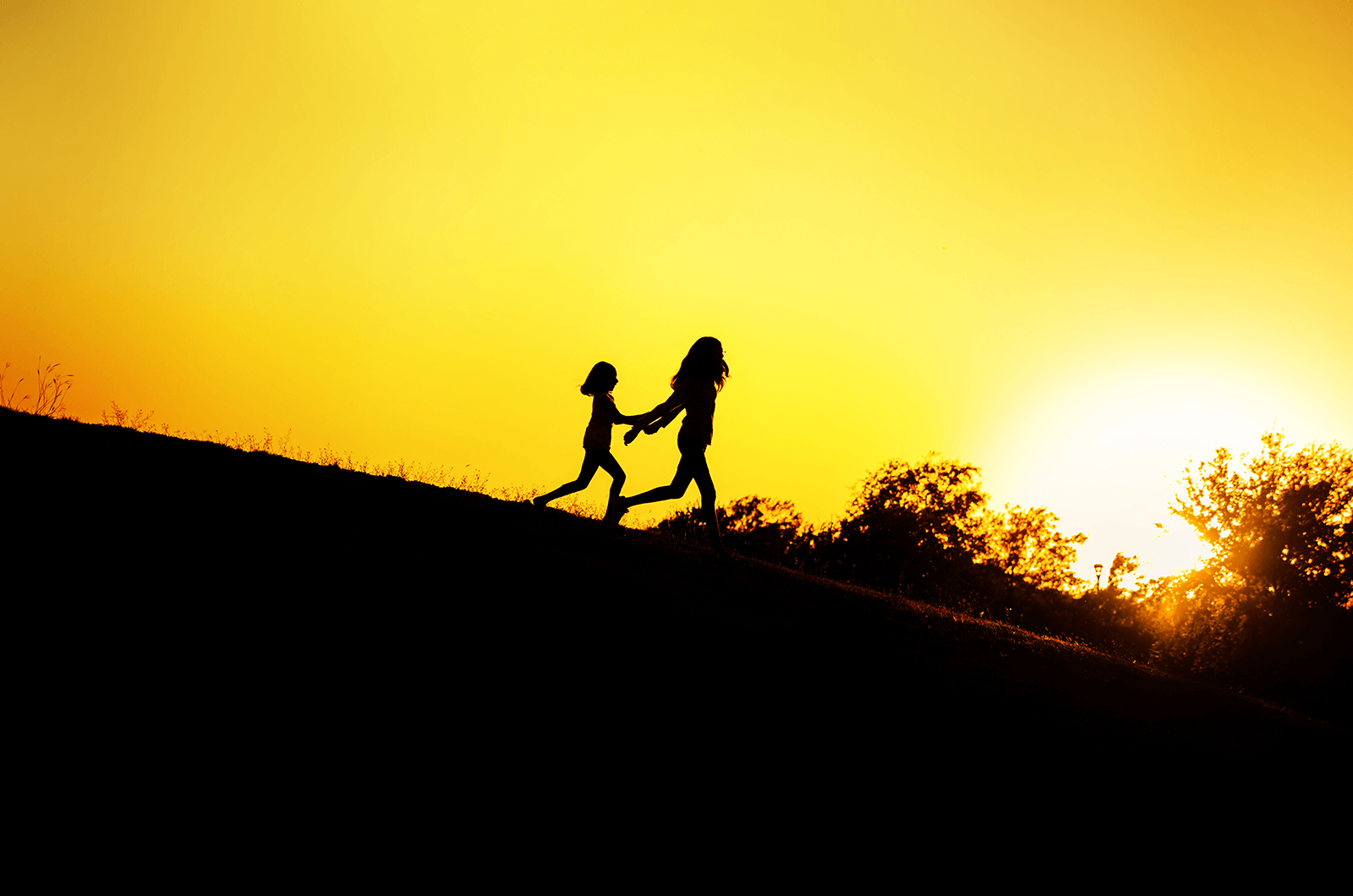 Silhouette of two kids running on hill while sun sets