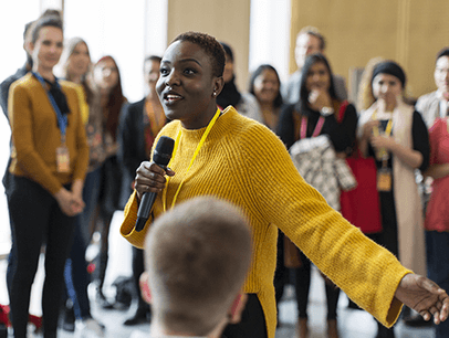 Woman in yellow sweater holding microphone speaking to audience