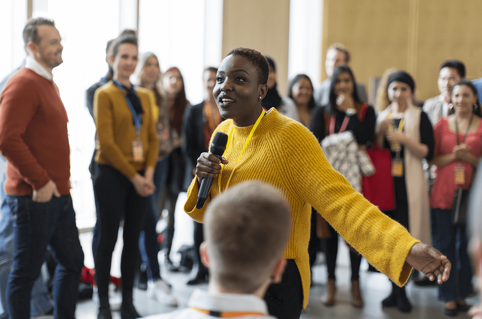 Woman in yellow sweater holding microphone speaking to audience