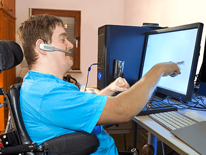 Man wearing blue shirt sitting in wheelchair pointing at computer screen