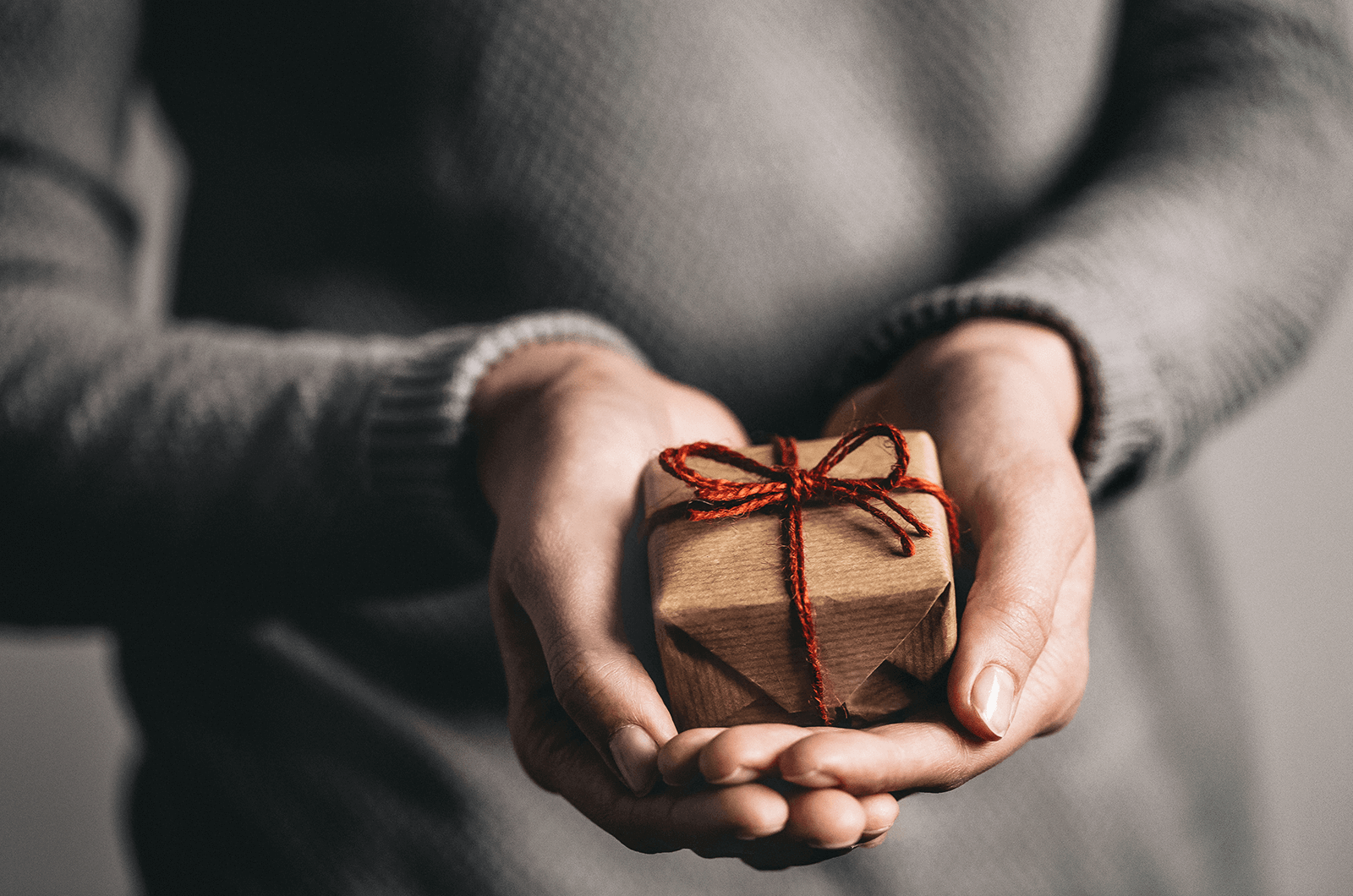 Two hands holding a small gift box with tied red bow