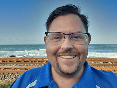 Man in glasses and blue shirt standing near ocean