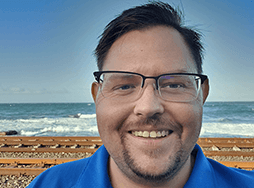 Man in glasses and blue shirt standing near ocean