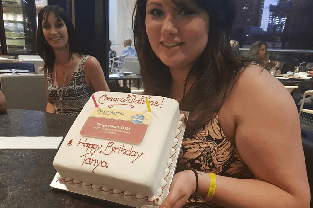 Tanya holds up a Toastmasters-themed cake for her birthday.