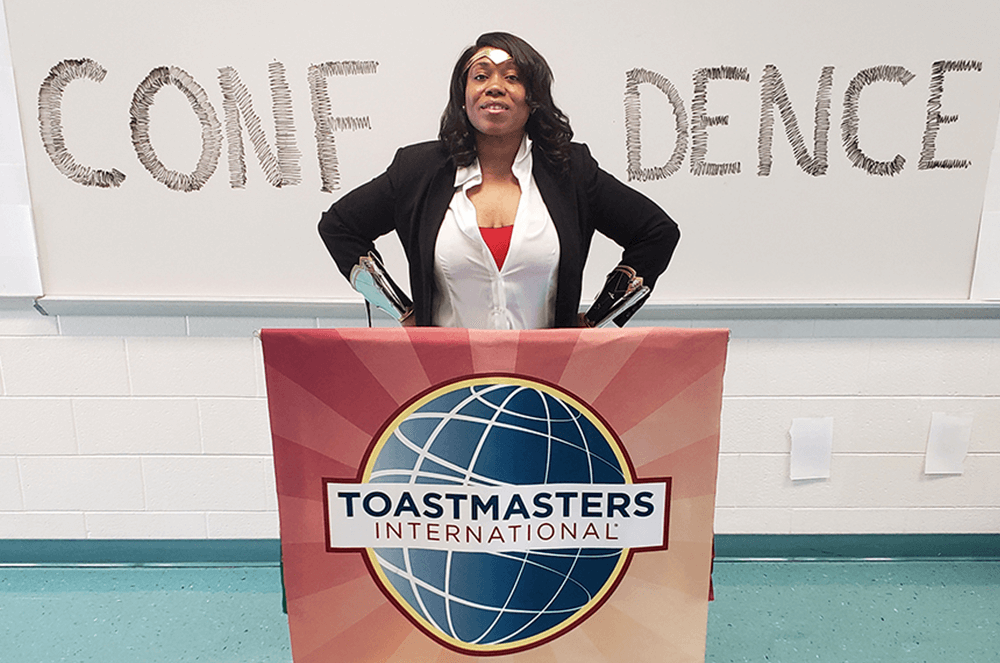 Woman in superwoman pose with Toastmasters banner