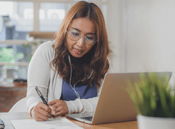 Woman taking notes while watching laptop