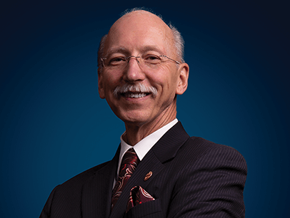 Richard Peck smiling in suit jacket and red tie