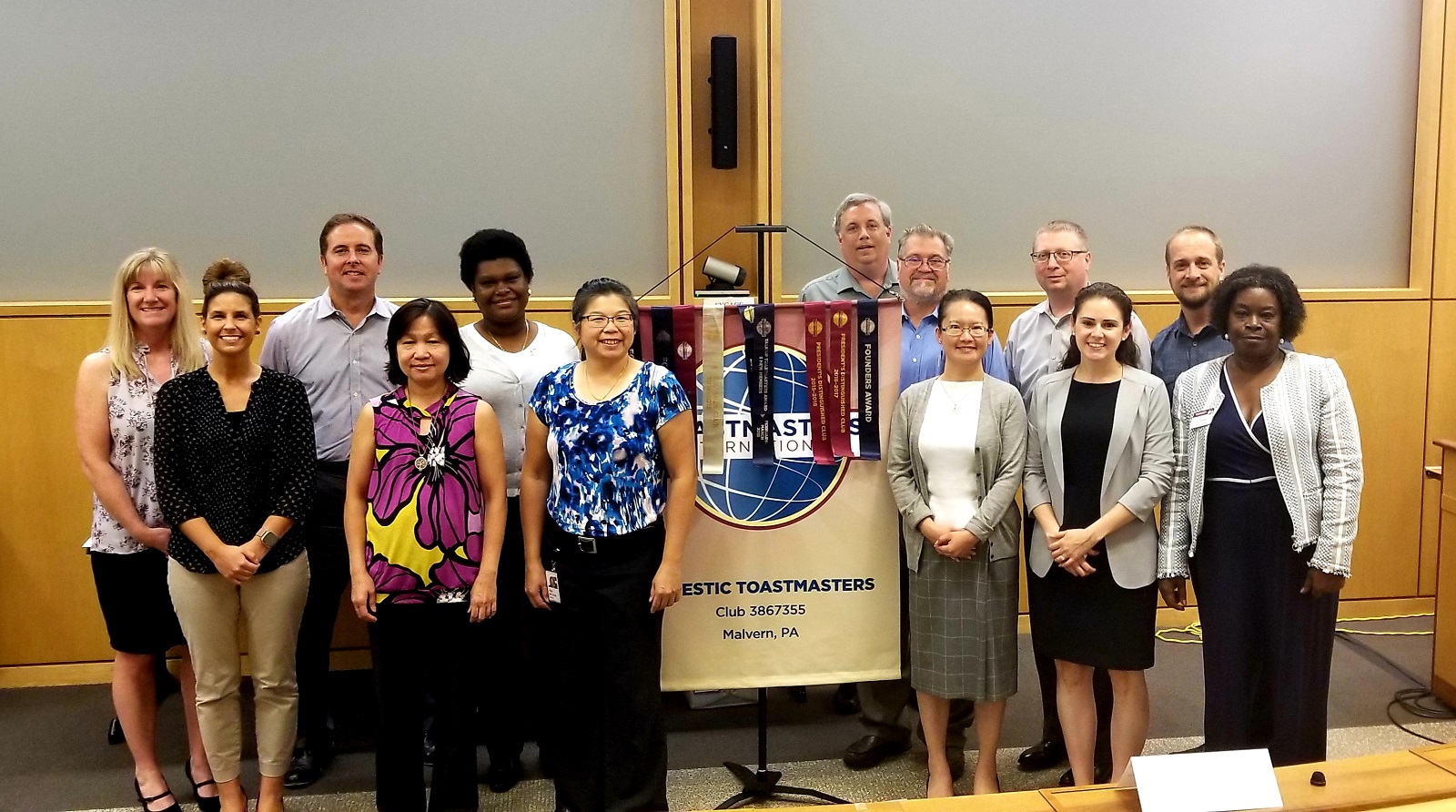 The diverse members of the Majestic Toastmasters club in Malvern, Pennsylvania, pose proudly with their club banner.